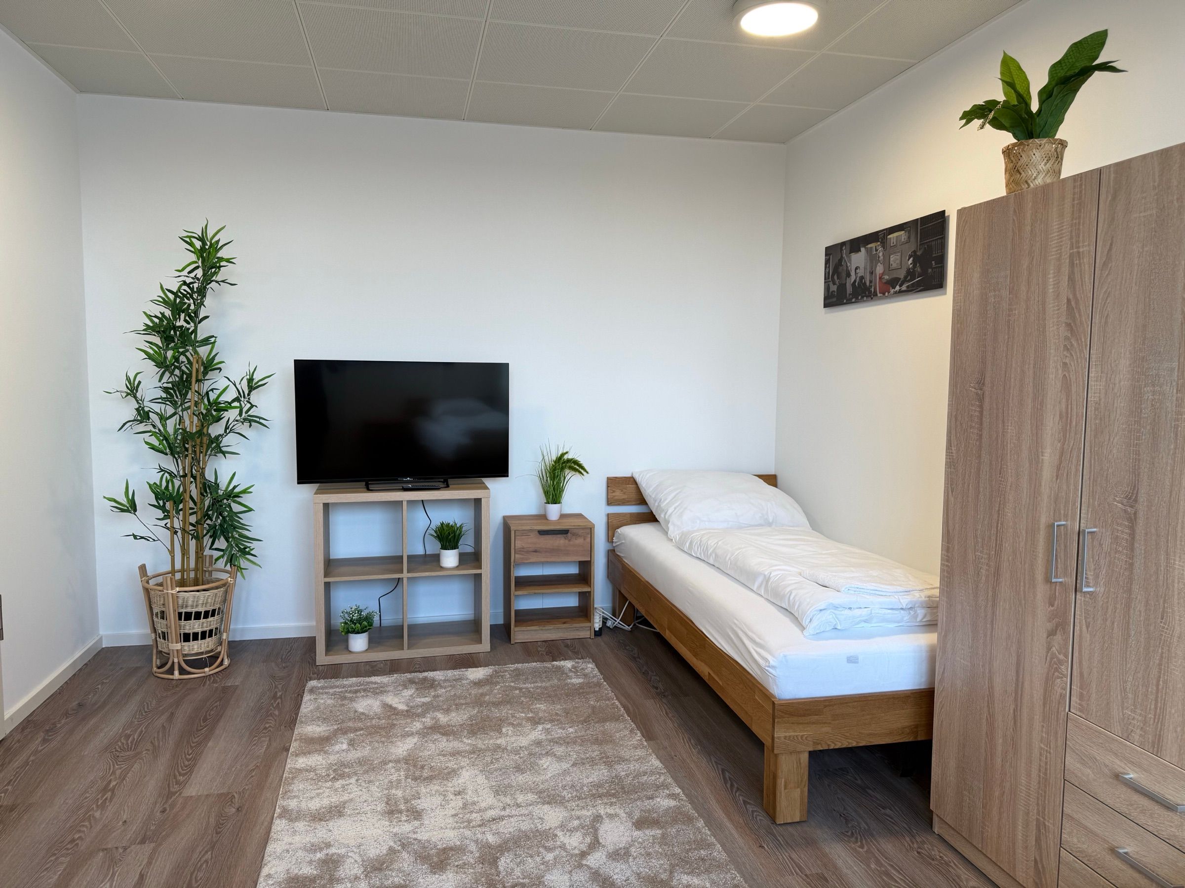 Wohnbereich mit Einzelbett, Fernseher und Kleiderschrank in einem möblierten MA-Flats Apartment