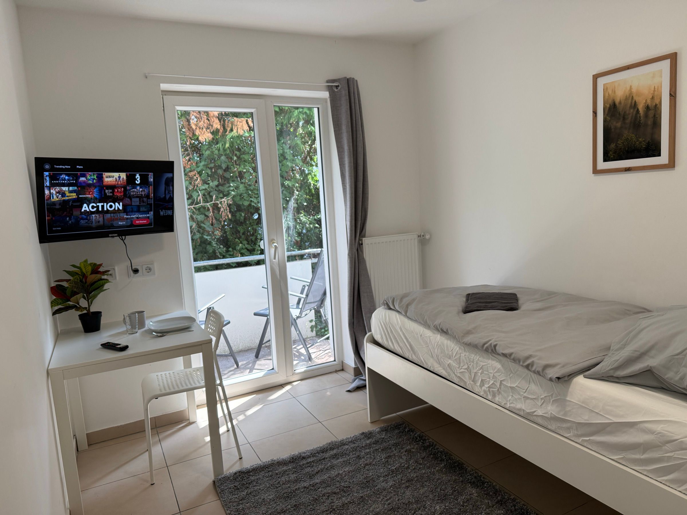 Einzelzimmer mit Balkontür, Schreibtisch und Fernseher in einem MA-Flats Apartment