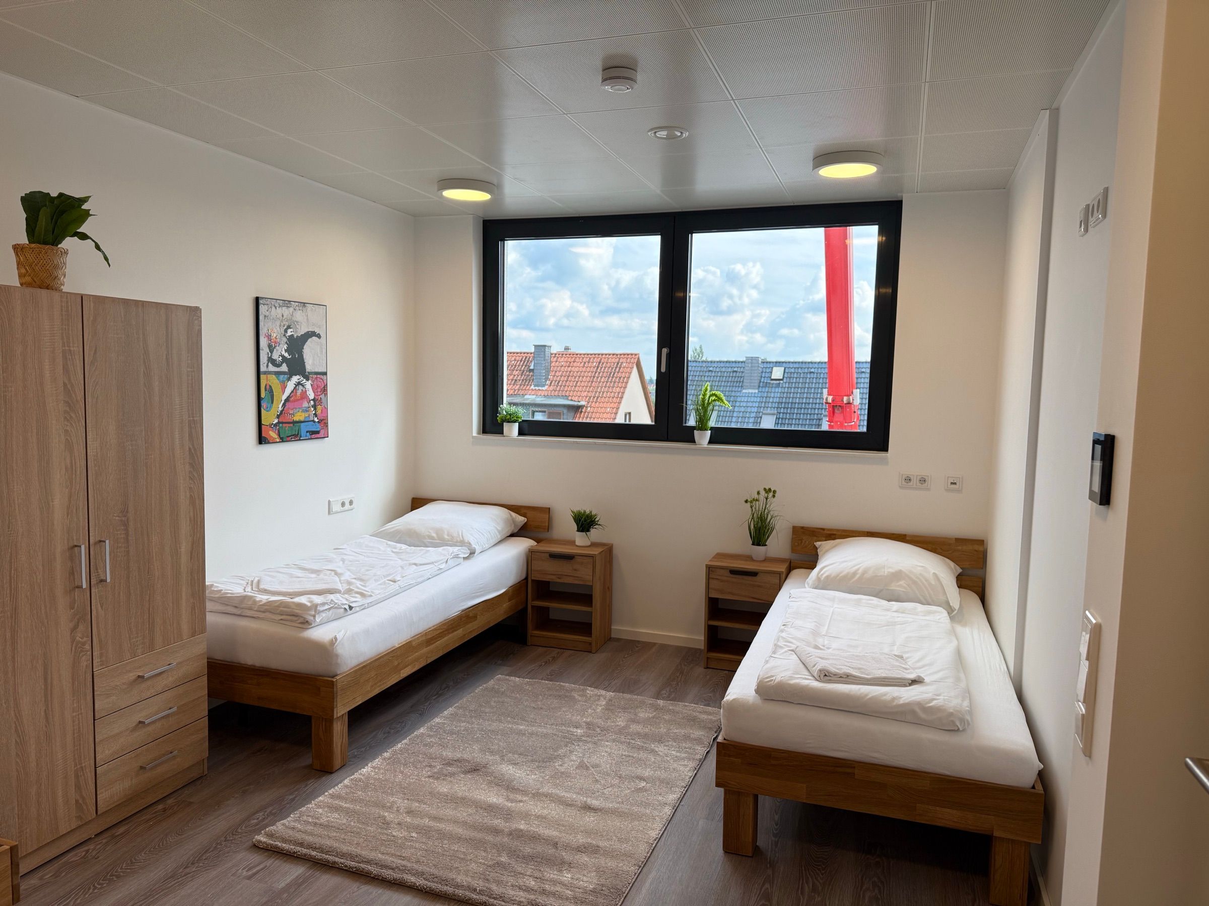 Helles Zweibettzimmer mit gemachten Betten und Fensterblick in einem MA-Flats Apartment